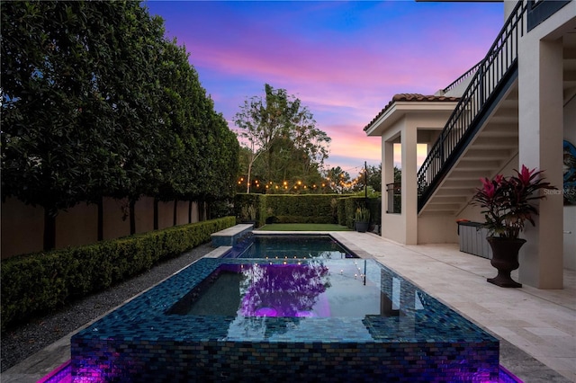 pool at dusk with a patio area and an in ground hot tub