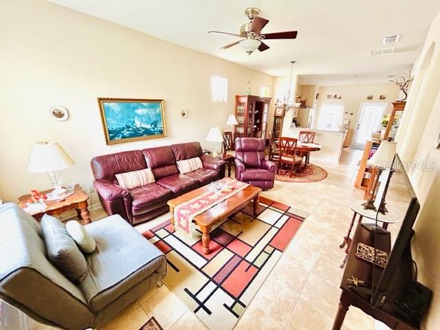 tiled living room with ceiling fan with notable chandelier