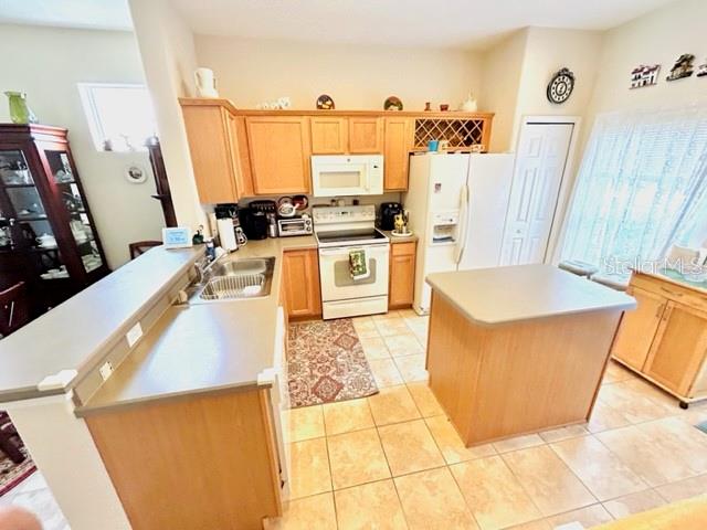 kitchen featuring kitchen peninsula, light tile patterned floors, sink, a center island, and white appliances