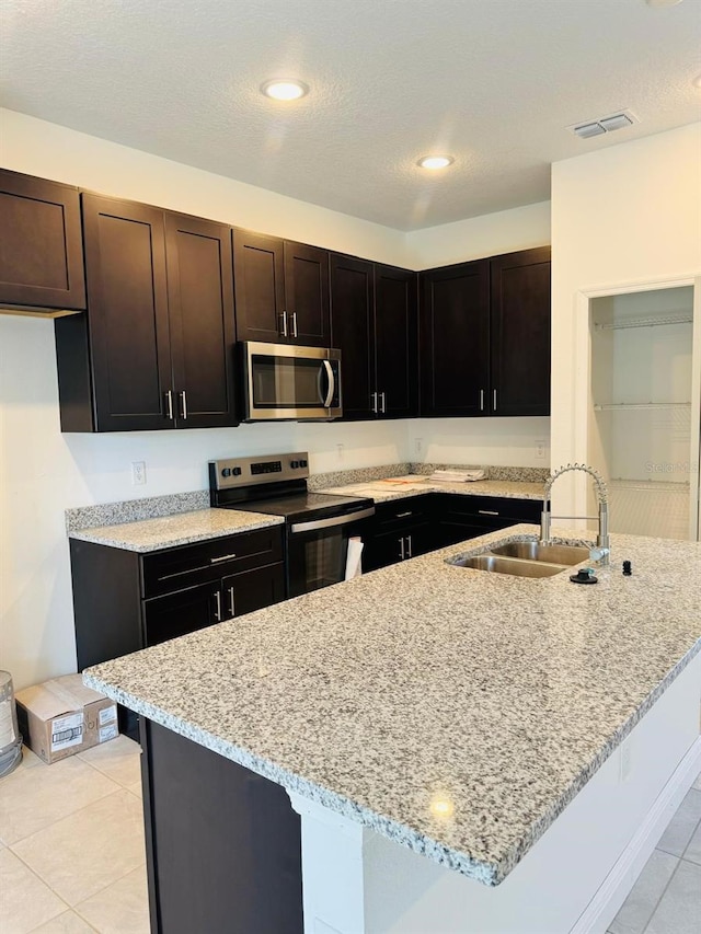 kitchen with light stone countertops, sink, dark brown cabinets, and stainless steel appliances