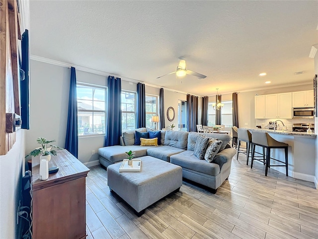 living room with crown molding, a textured ceiling, sink, light hardwood / wood-style floors, and ceiling fan