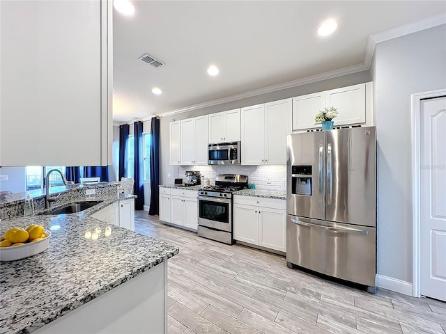 kitchen featuring stainless steel appliances, light stone counters, crown molding, white cabinetry, and light hardwood / wood-style flooring