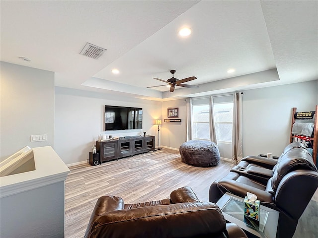 living room featuring ceiling fan, a raised ceiling, and light hardwood / wood-style flooring