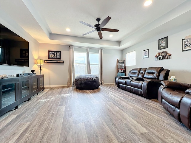 living room with light wood-type flooring, ceiling fan, and a raised ceiling