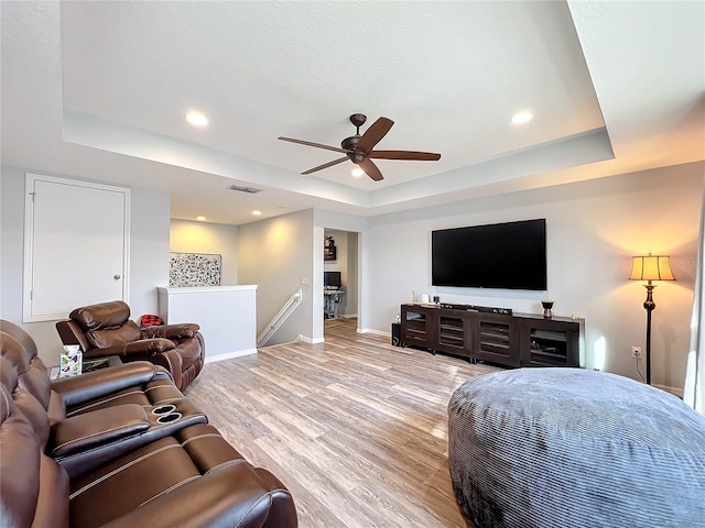 living room featuring light hardwood / wood-style floors, ceiling fan, and a tray ceiling