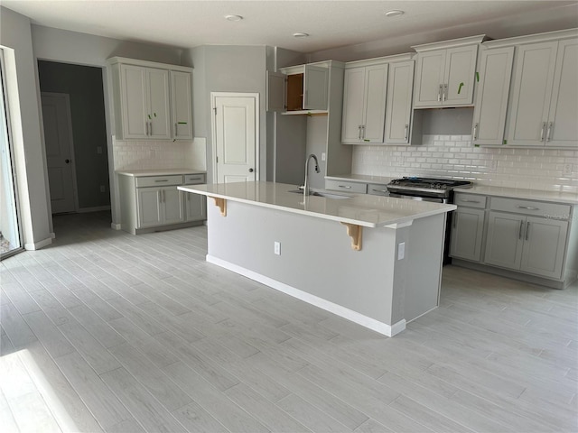 kitchen with gray cabinetry, sink, an island with sink, and a breakfast bar