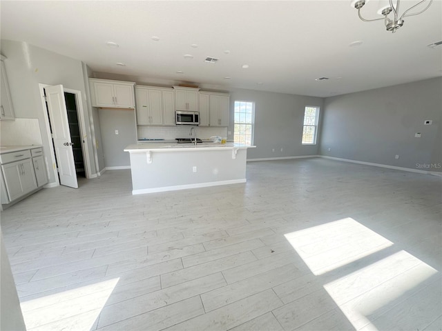 kitchen with baseboards, stainless steel microwave, open floor plan, light countertops, and backsplash