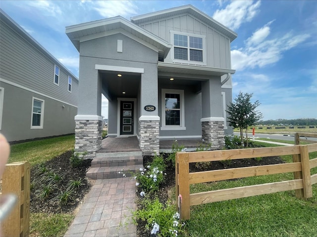 view of front of property with a porch, stone siding, board and batten siding, stucco siding, and fence