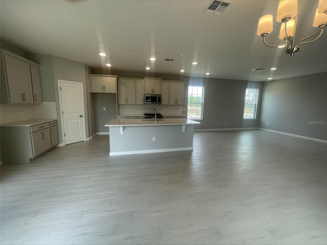kitchen featuring stainless steel microwave, decorative backsplash, a center island with sink, visible vents, and open floor plan