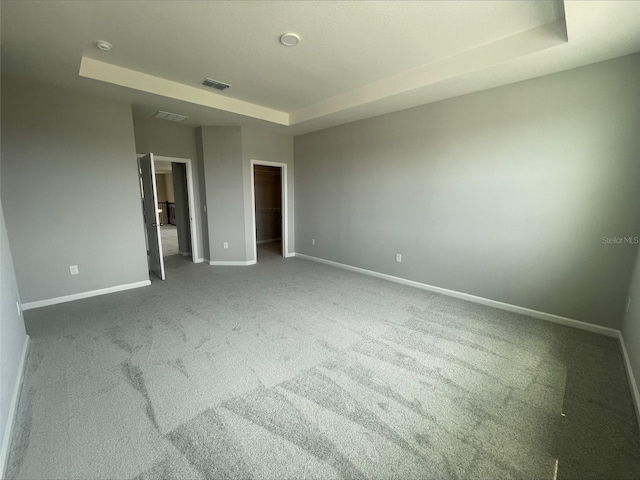 unfurnished bedroom with a raised ceiling, a walk in closet, visible vents, baseboards, and carpet floors