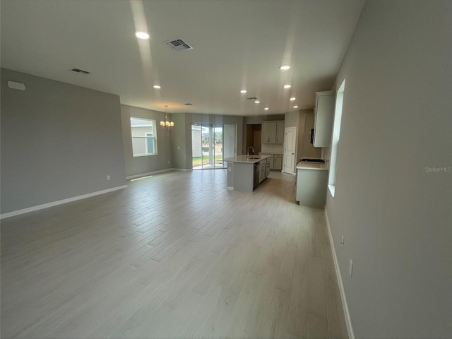 unfurnished living room with recessed lighting, a sink, light wood-style floors, a notable chandelier, and baseboards