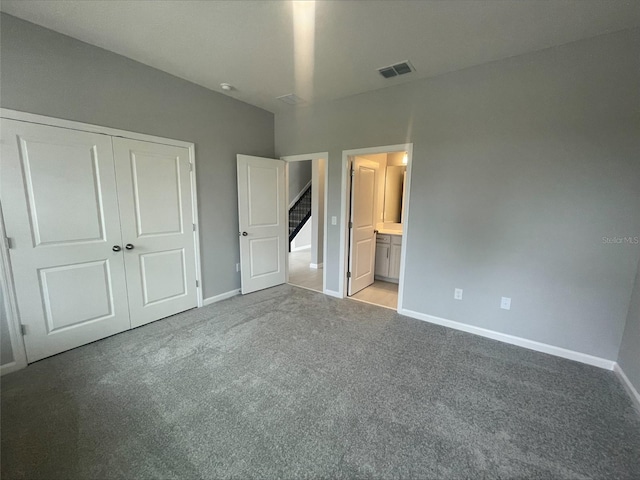 unfurnished bedroom with a closet, light carpet, ensuite bathroom, baseboards, and visible vents