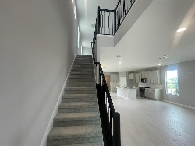 staircase featuring visible vents, baseboards, recessed lighting, a towering ceiling, and wood finished floors