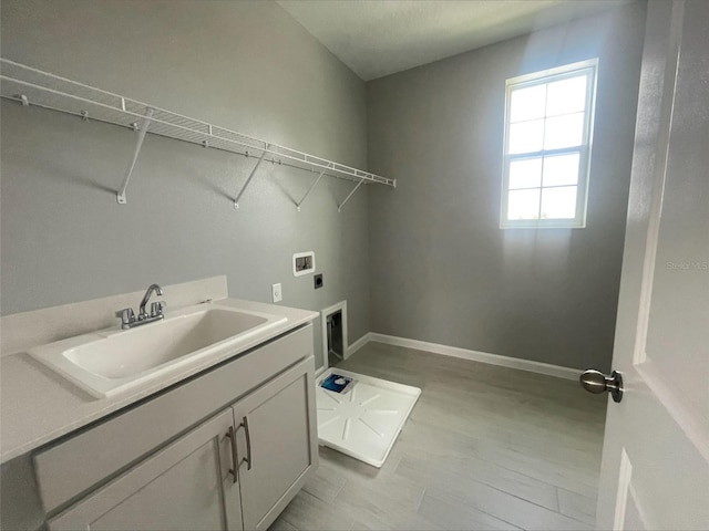 washroom featuring electric dryer hookup, baseboards, cabinet space, and a sink