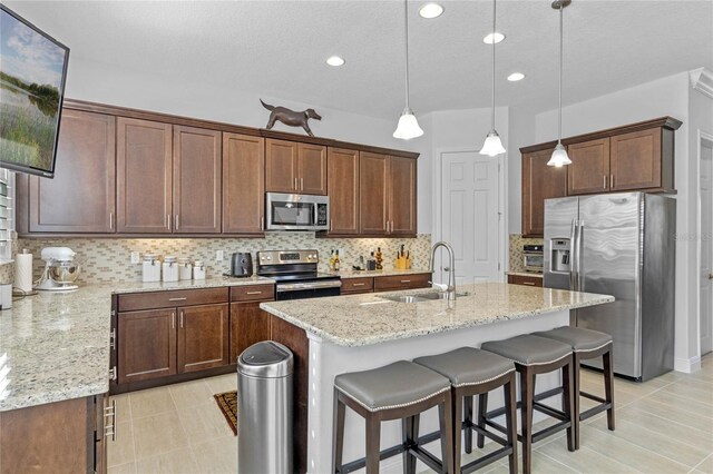 kitchen featuring appliances with stainless steel finishes, decorative light fixtures, decorative backsplash, sink, and an island with sink