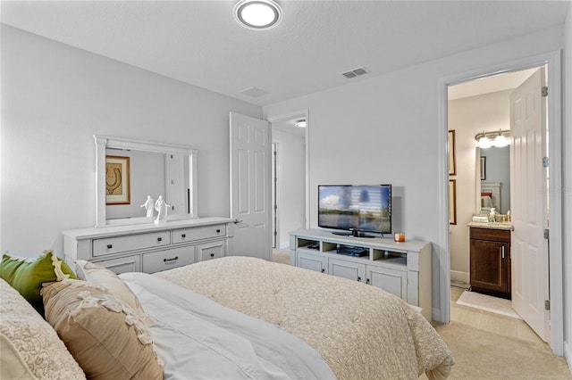 bedroom with a textured ceiling, light colored carpet, and ensuite bathroom