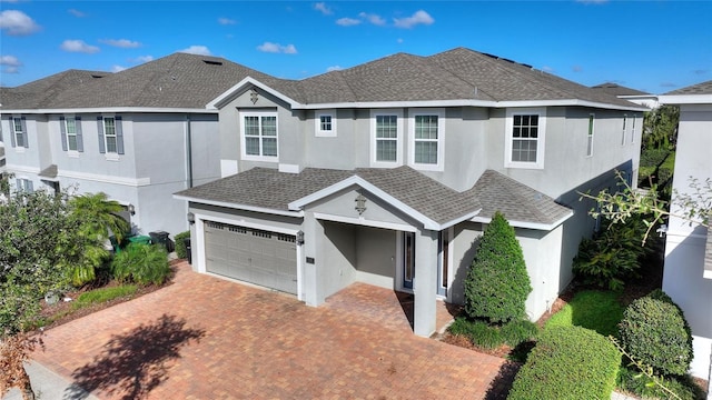 view of front of property with a shingled roof, decorative driveway, an attached garage, and stucco siding