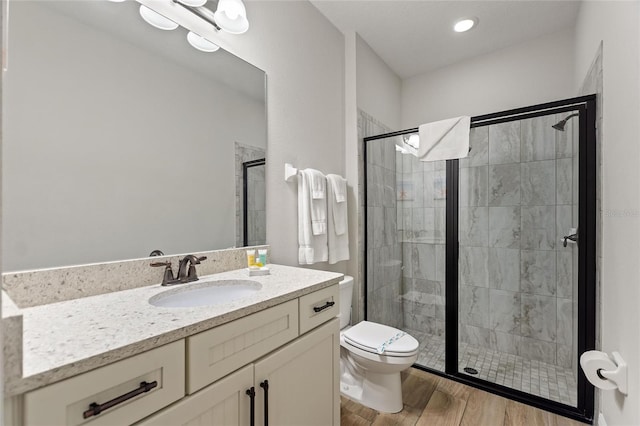 bathroom with hardwood / wood-style flooring, a shower with shower door, vanity, and toilet