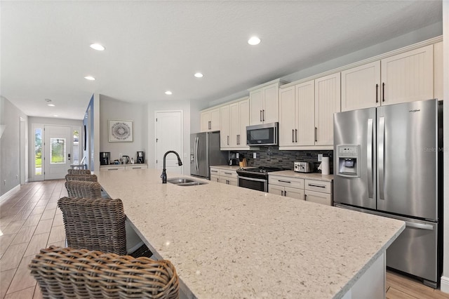 kitchen featuring appliances with stainless steel finishes, sink, a center island with sink, and light hardwood / wood-style flooring