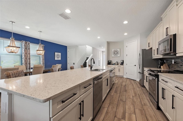 kitchen with a center island with sink, sink, white cabinetry, appliances with stainless steel finishes, and light hardwood / wood-style flooring