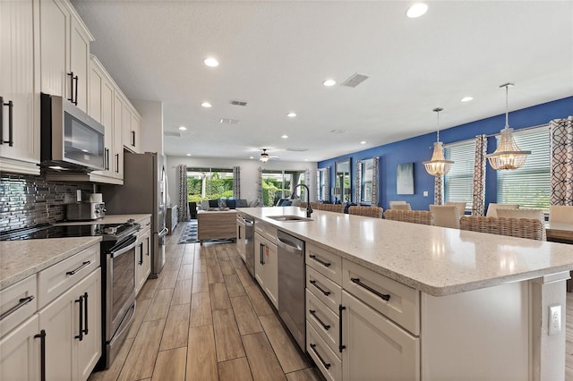 kitchen featuring stainless steel appliances, white cabinetry, a large island with sink, sink, and pendant lighting