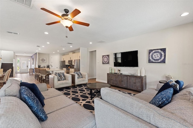 living room with light wood-type flooring, a textured ceiling, and ceiling fan