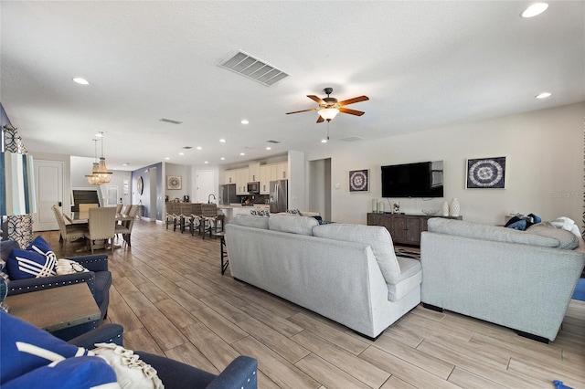 living room featuring ceiling fan with notable chandelier and light hardwood / wood-style flooring