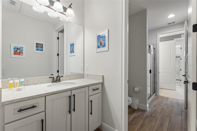 bathroom with hardwood / wood-style flooring, a shower with door, vanity, and toilet