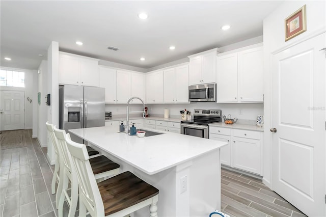 kitchen with appliances with stainless steel finishes, a breakfast bar, sink, a center island with sink, and white cabinetry