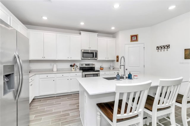 kitchen with stainless steel appliances, white cabinetry, a center island with sink, and sink