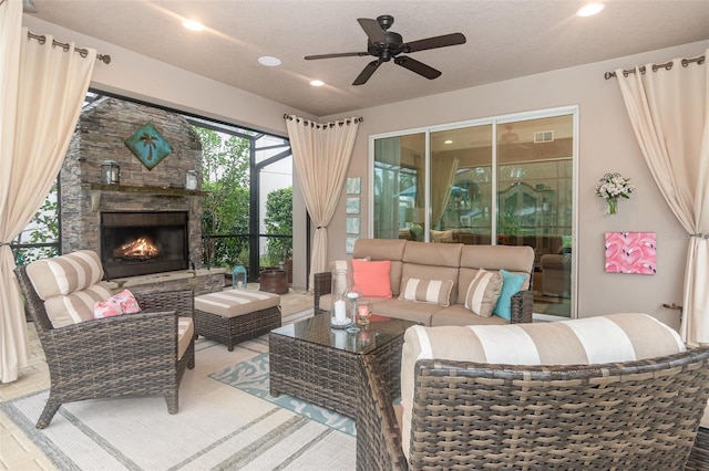 living room with ceiling fan, a textured ceiling, and an outdoor stone fireplace