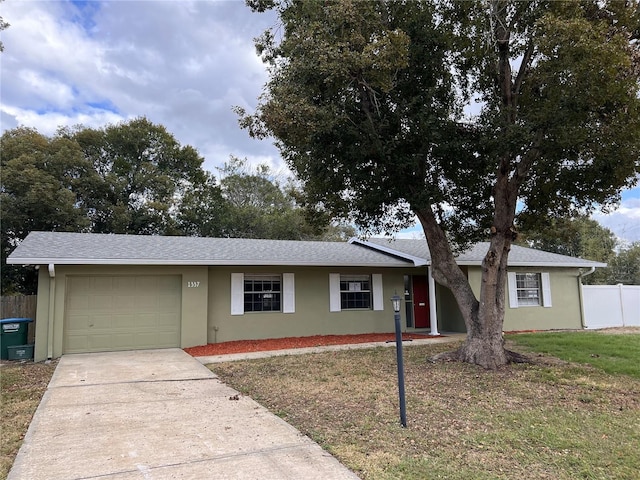 ranch-style home with a garage, fence, driveway, stucco siding, and a front yard