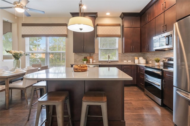 kitchen with tasteful backsplash, stainless steel appliances, a kitchen island, dark brown cabinetry, and dark hardwood / wood-style flooring