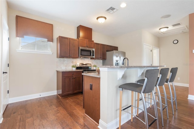 kitchen featuring stainless steel appliances, a center island with sink, a kitchen breakfast bar, dark hardwood / wood-style floors, and backsplash