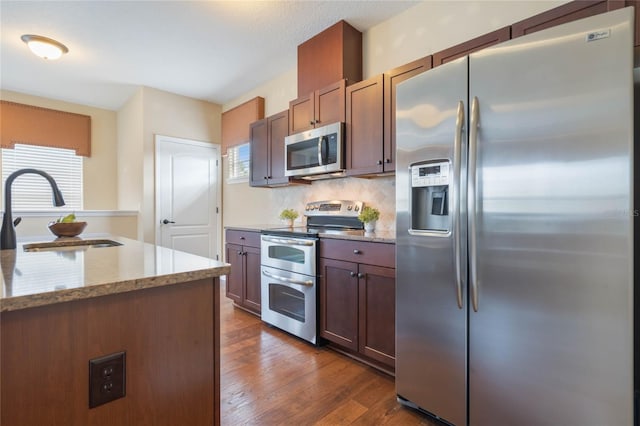 kitchen with dark wood-type flooring, a wealth of natural light, light stone counters, and stainless steel appliances