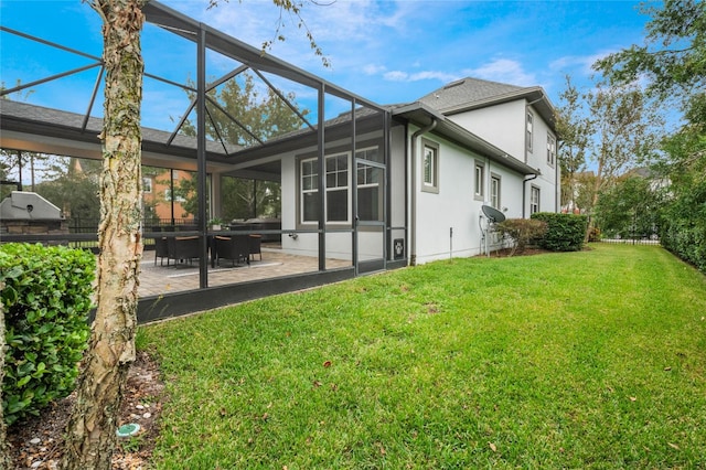 back of house featuring a lawn, glass enclosure, and a patio area