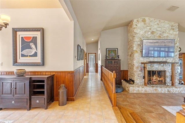 hall with wooden walls, light tile patterned floors, and vaulted ceiling