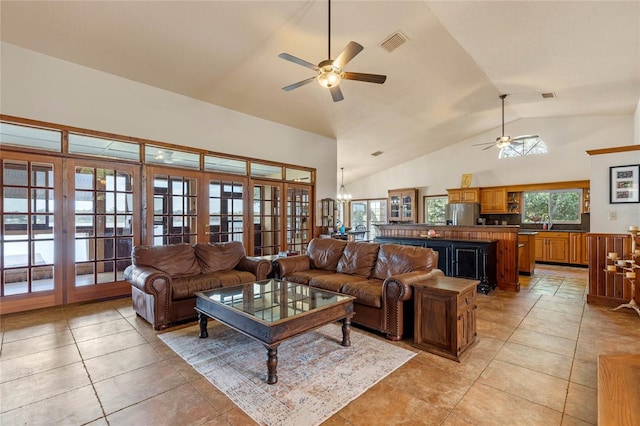 tiled living room with high vaulted ceiling, french doors, and ceiling fan with notable chandelier