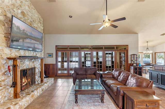 living room with a stone fireplace, french doors, ceiling fan with notable chandelier, wood walls, and a textured ceiling