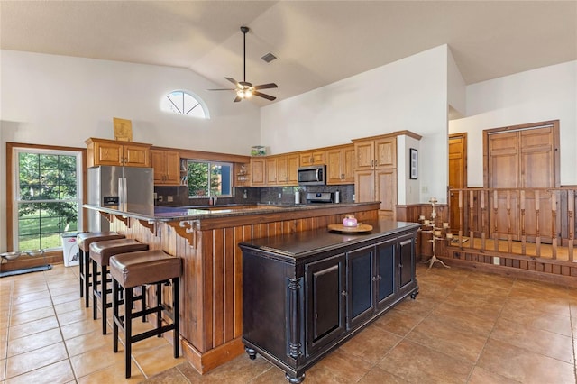 kitchen with stainless steel appliances, high vaulted ceiling, light tile patterned flooring, a kitchen island, and backsplash