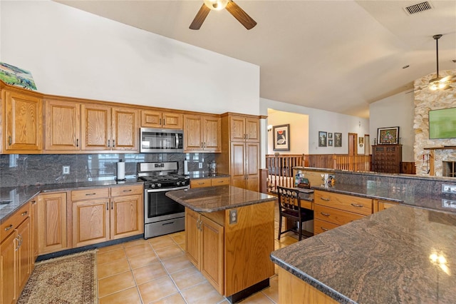 kitchen with light tile patterned floors, ceiling fan, a kitchen island, appliances with stainless steel finishes, and dark stone countertops