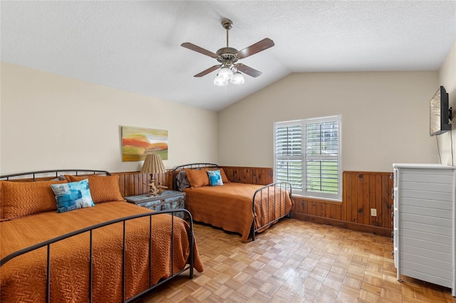 bedroom featuring ceiling fan, wooden walls, a textured ceiling, and lofted ceiling