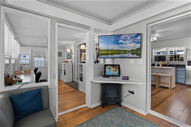 home office featuring ceiling fan, wood-type flooring, a wood stove, and a textured ceiling