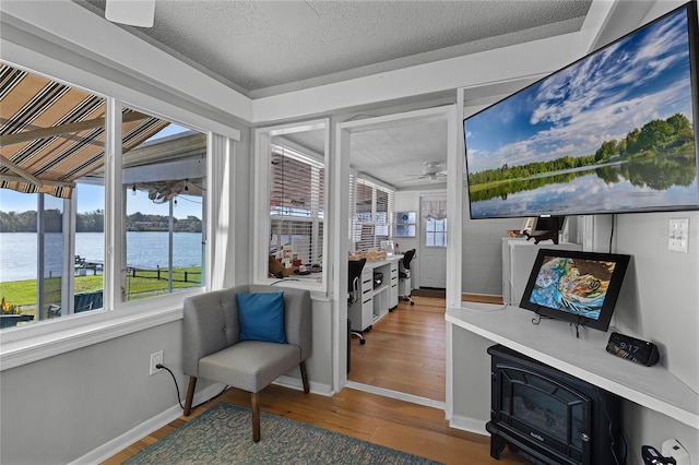 living area featuring a water view, wood-type flooring, ceiling fan, and a textured ceiling