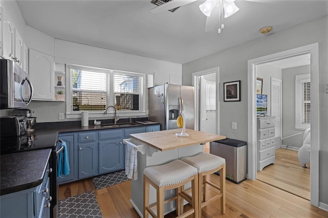 kitchen featuring light hardwood / wood-style floors, blue cabinets, sink, a breakfast bar, and appliances with stainless steel finishes