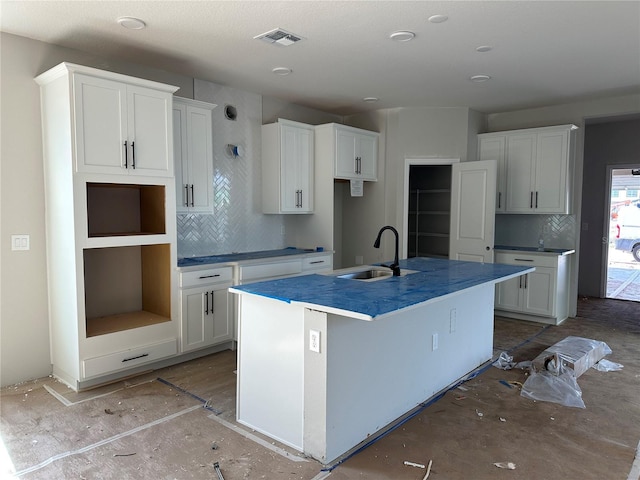 kitchen with sink, backsplash, white cabinetry, and an island with sink