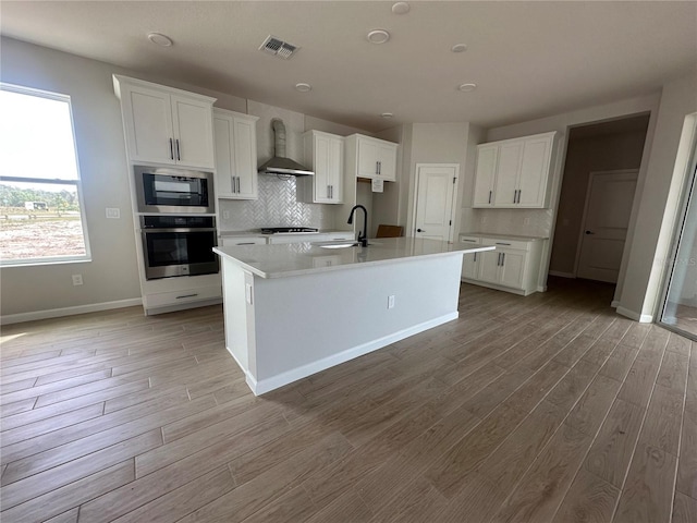 kitchen with a sink, visible vents, stainless steel oven, built in microwave, and wall chimney exhaust hood