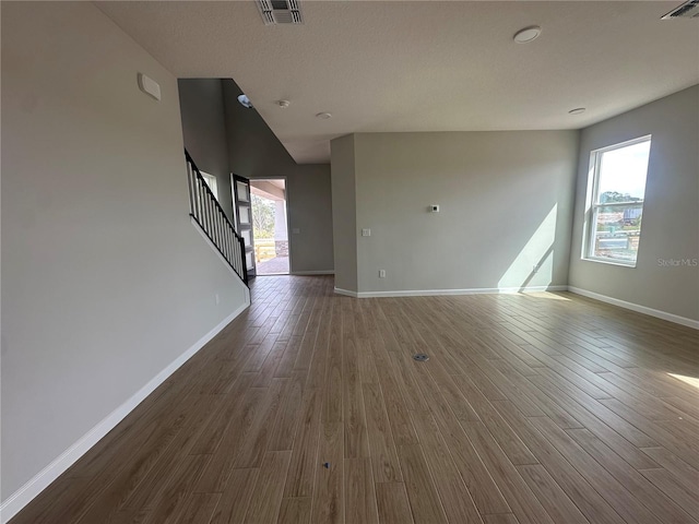 unfurnished living room with stairway, dark wood finished floors, visible vents, and a healthy amount of sunlight