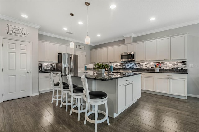 kitchen featuring a center island with sink, crown molding, stainless steel appliances, dark hardwood / wood-style flooring, and white cabinets