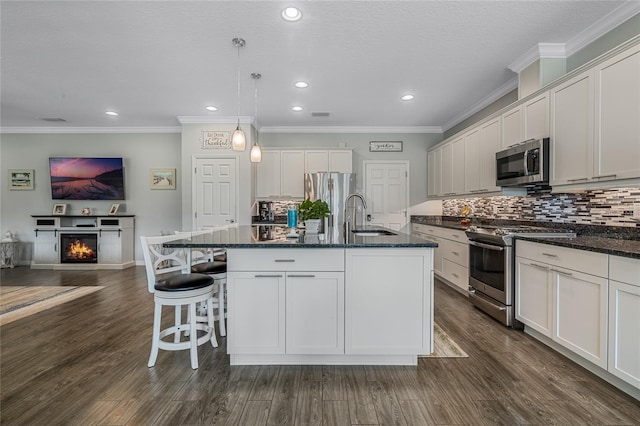 kitchen featuring dark wood-type flooring, appliances with stainless steel finishes, decorative light fixtures, and an island with sink